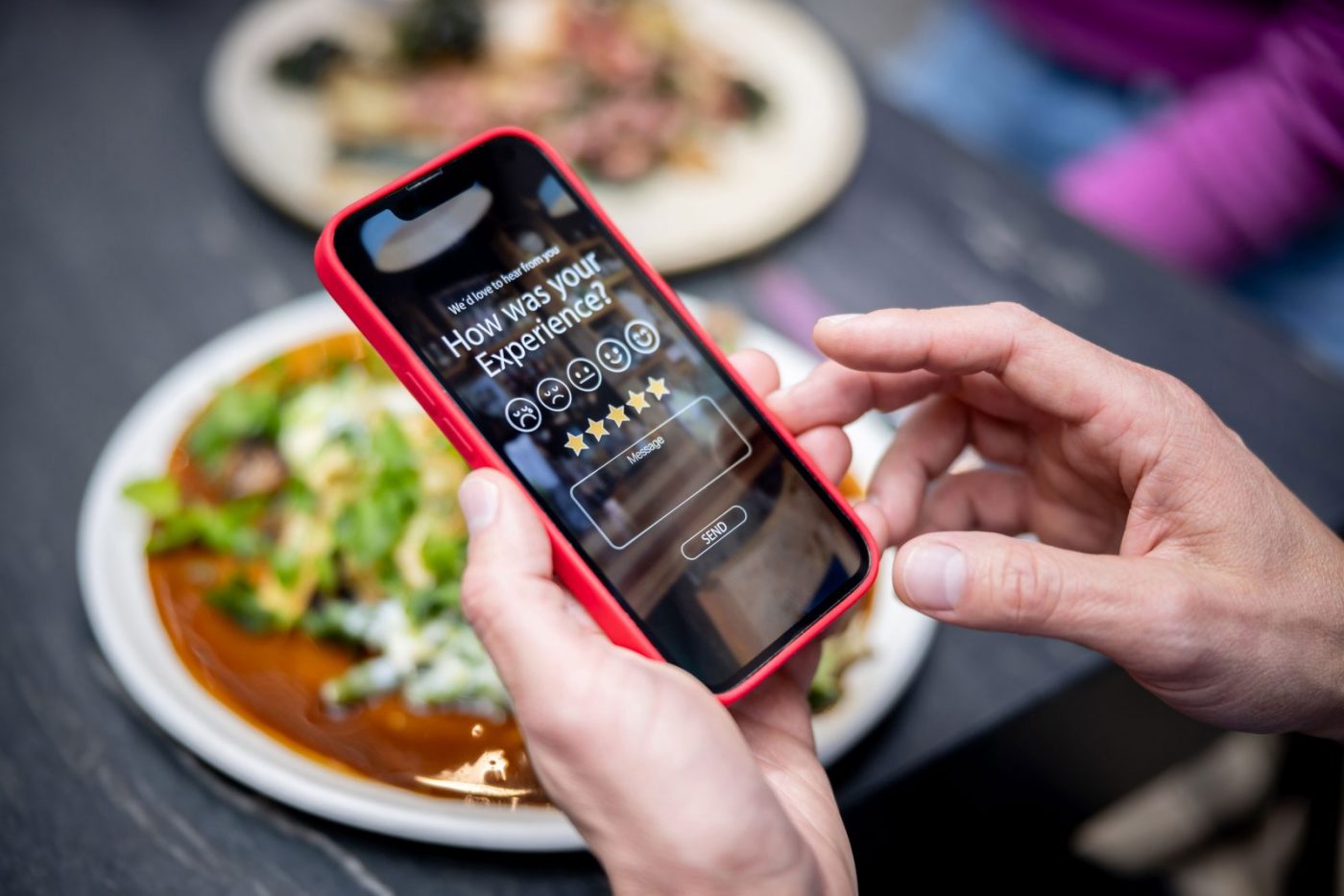 Hands holding a mobile phone. The phone is open on a review page asking to rate the business. Set in a retail food outlet.