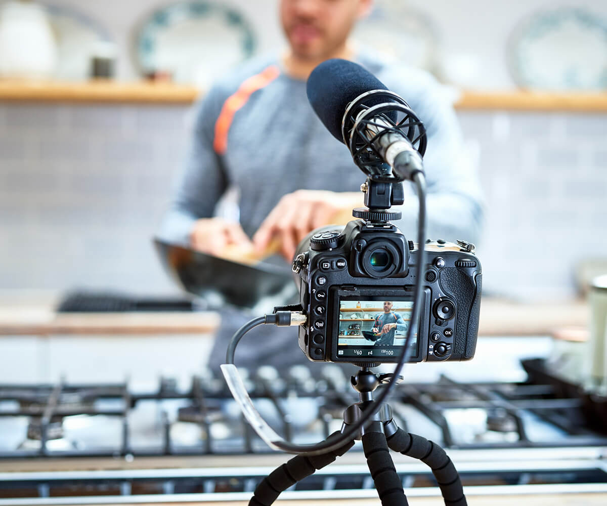 Camera with microphone filming man making food in kitchen