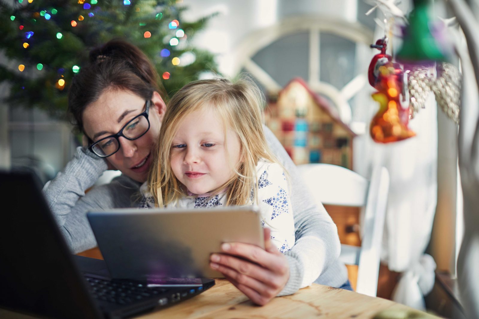 Woman and child sat by a Christmas tree looking excited at a tablet/ipad