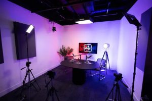 Image shows on of Reach Plc's new studios for video and podcast production. Image shows two chairs and a desk in the background with some foliage and lights and cameras facing them.