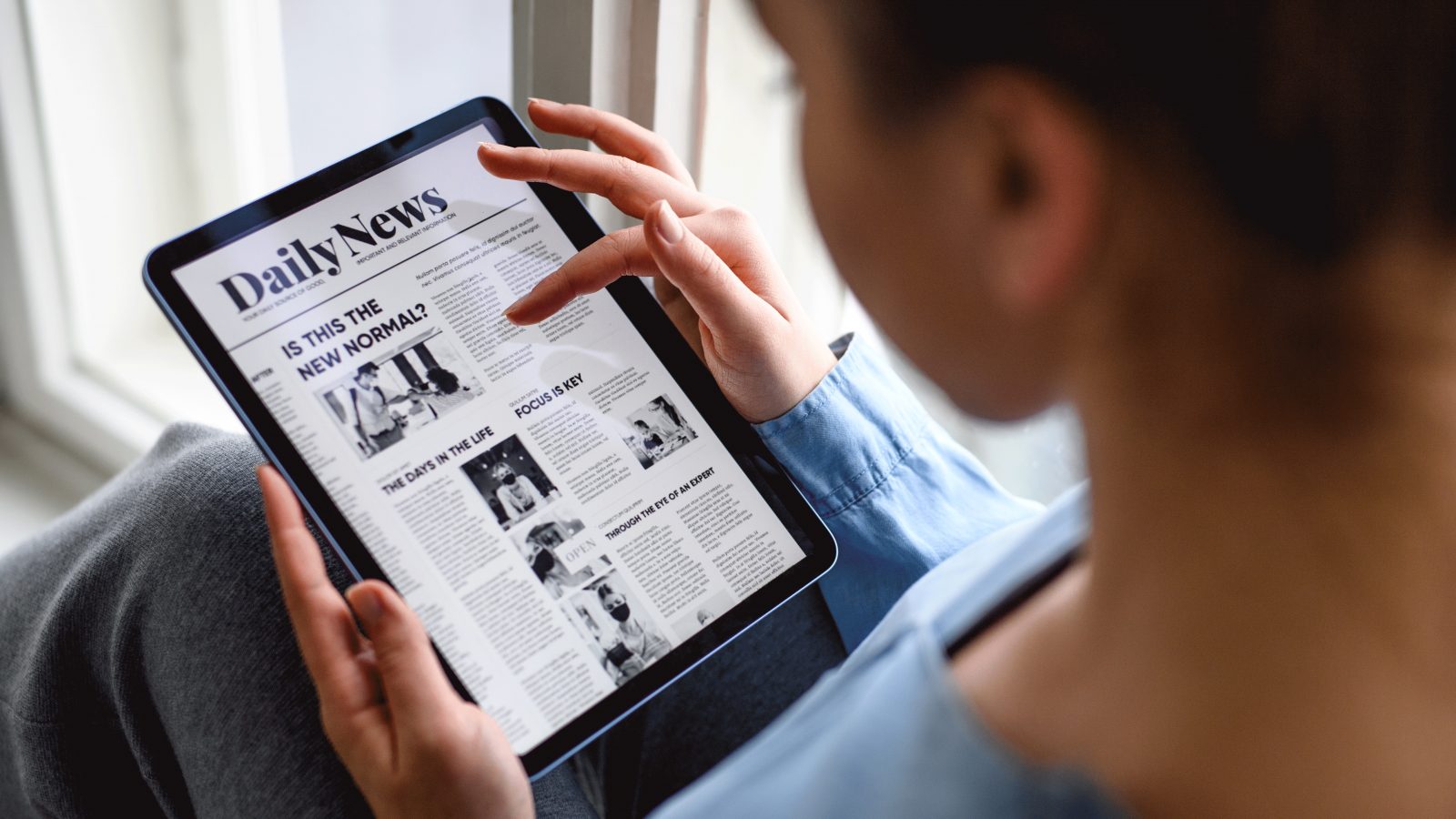 Young woman indoors at home, reading news on tablet. - stock photo Close-up of woman sitting and relaxing on window sill.