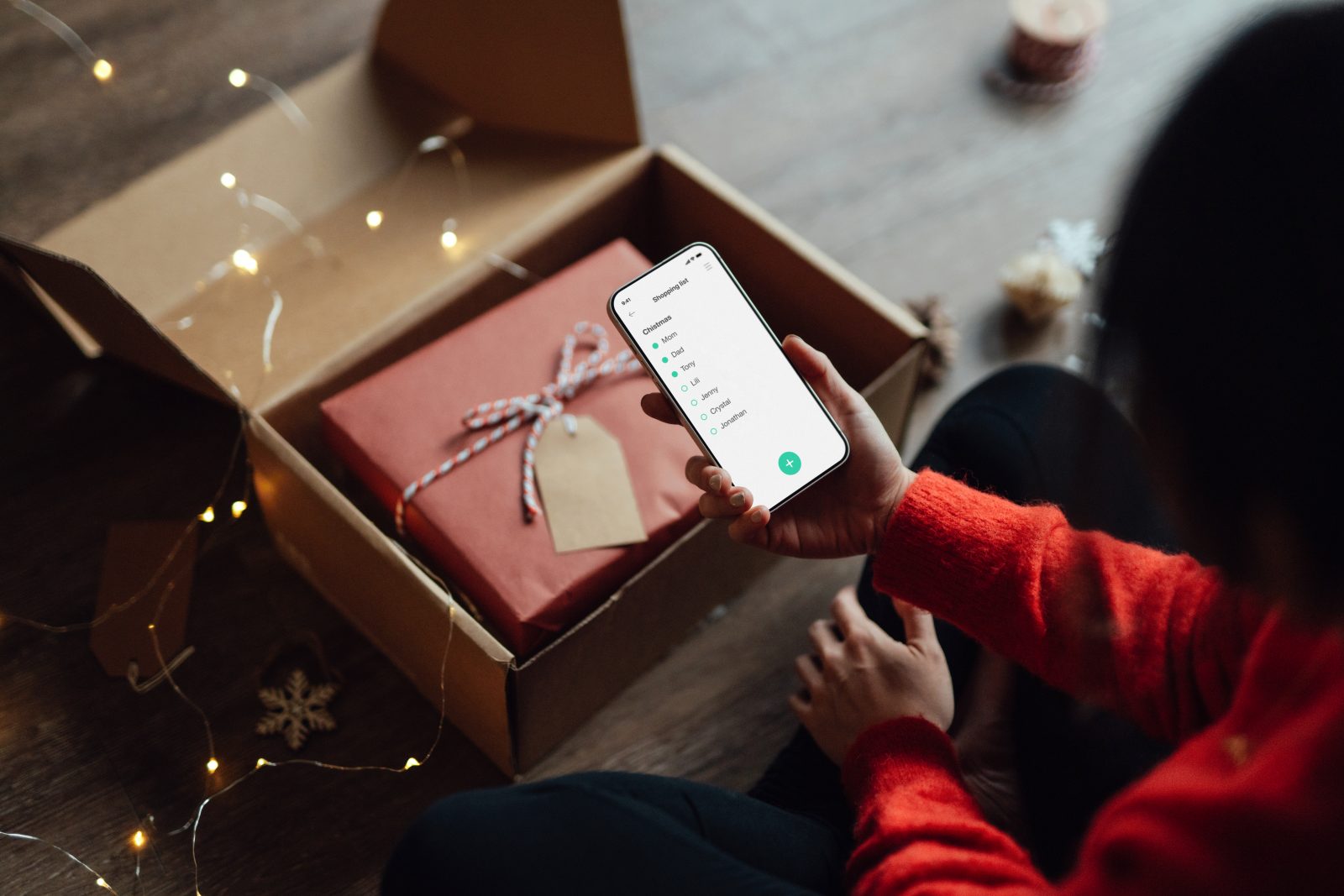 Close up shot of unrecognizable young Black woman sitting by the Christmas tree and rating her experience after doing online shopping via smart phone.